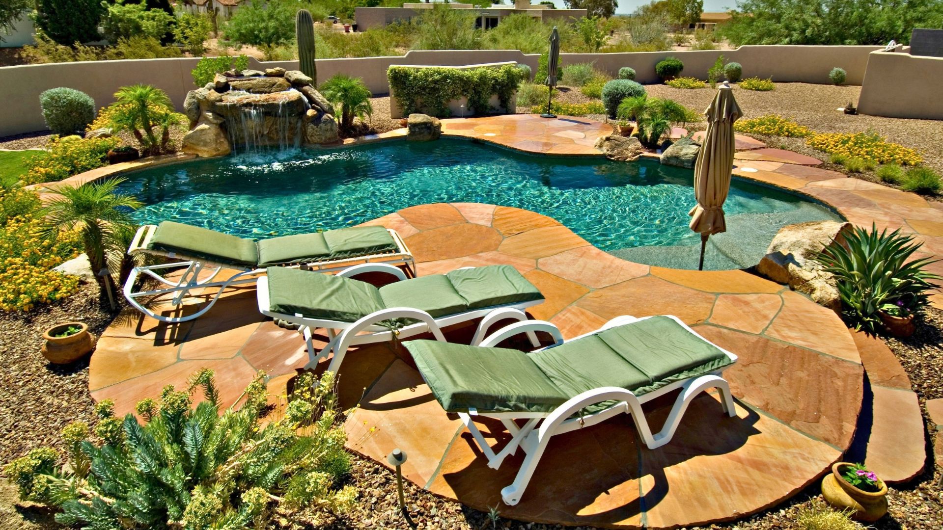 Freeform pool with flagstone deck, lounge chairs, rock waterfall, and desert-style plants.