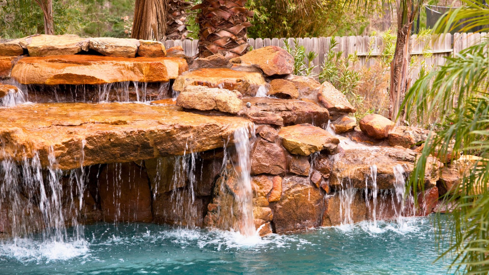 Natural stone waterfall flowing into a pool surrounded by palms.